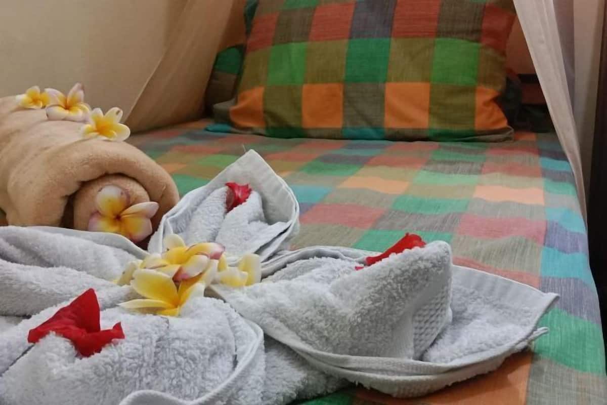 Un lit bien fait, recouvert d’une couverture à carreaux aux couleurs vives, avec une serviette enroulée et quelques fleurs.