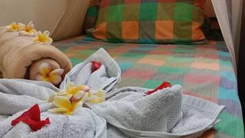 Una cama bien hecha con un colorido edredón de cuadros, una toalla enrollada y algunas flores.