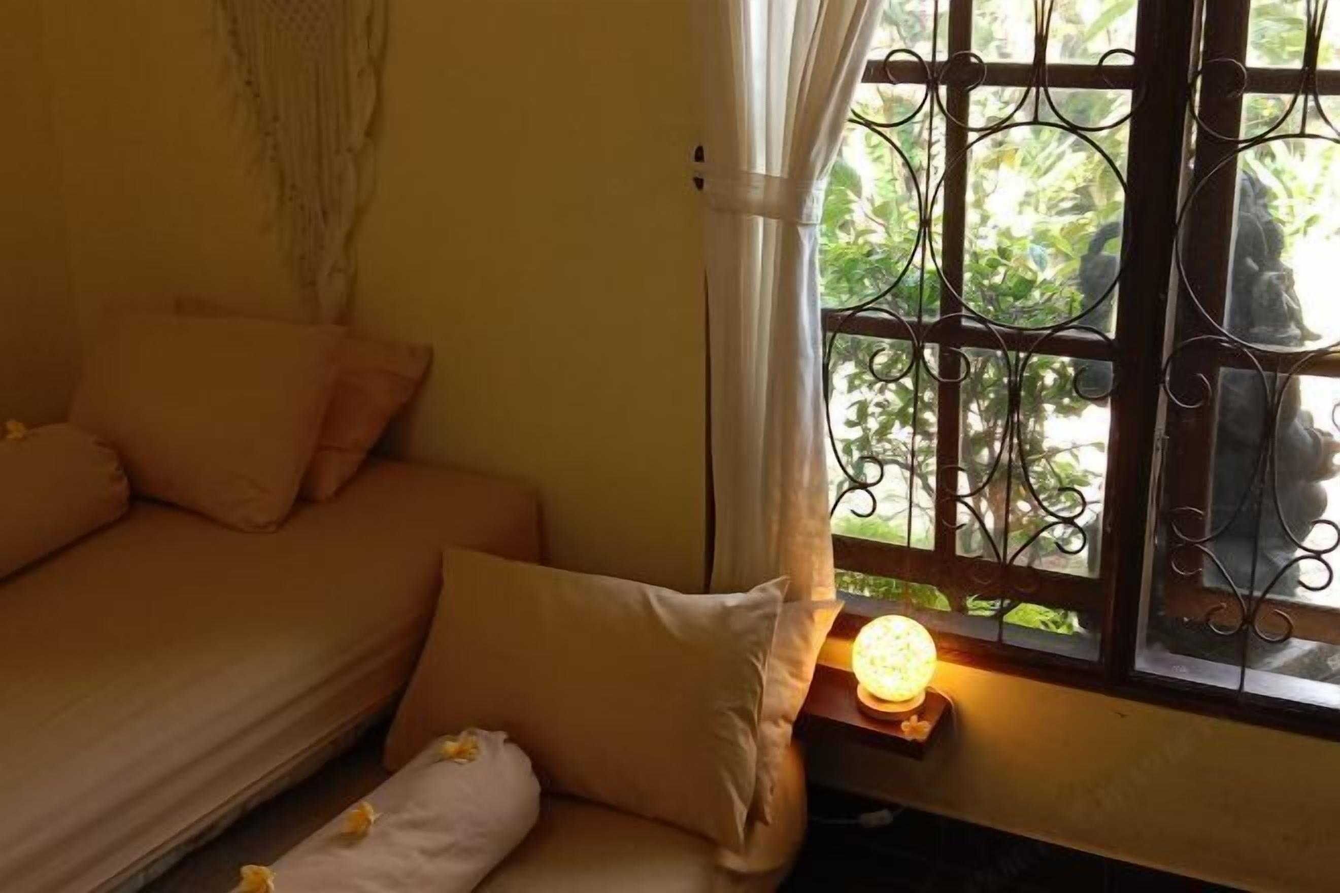 Una habitación con cama, ventana con rejas decorativas y una lámpara de noche.