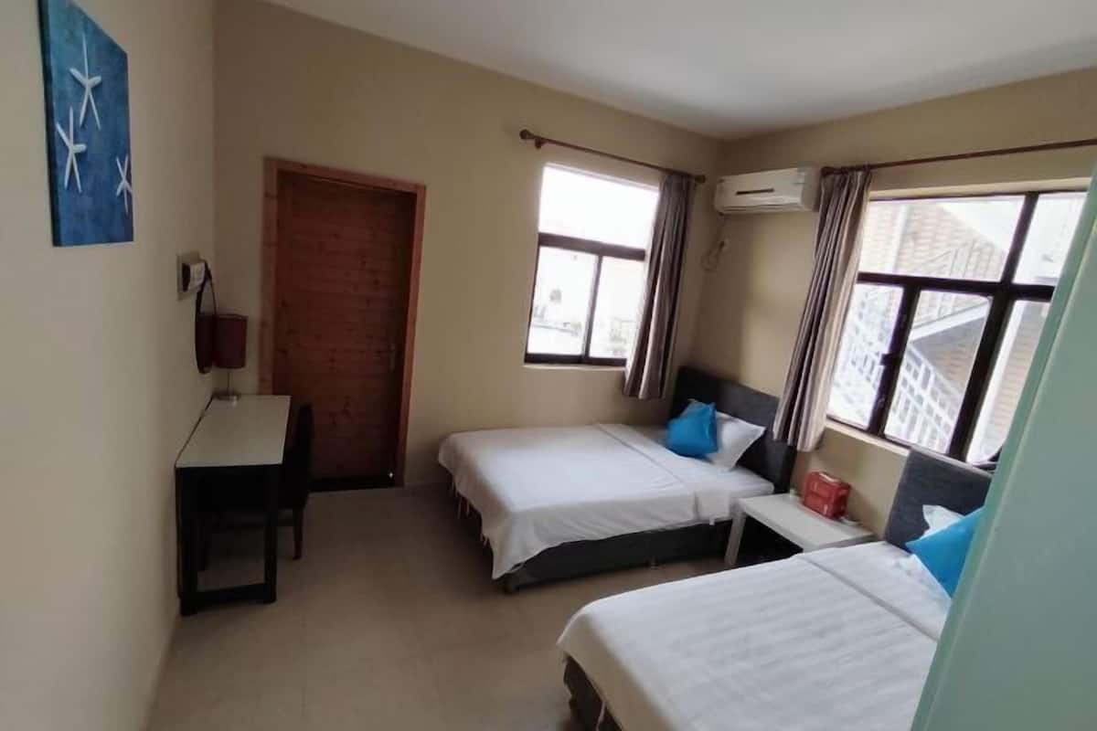 A room with two beds, a desk, a window with curtains, and a door.