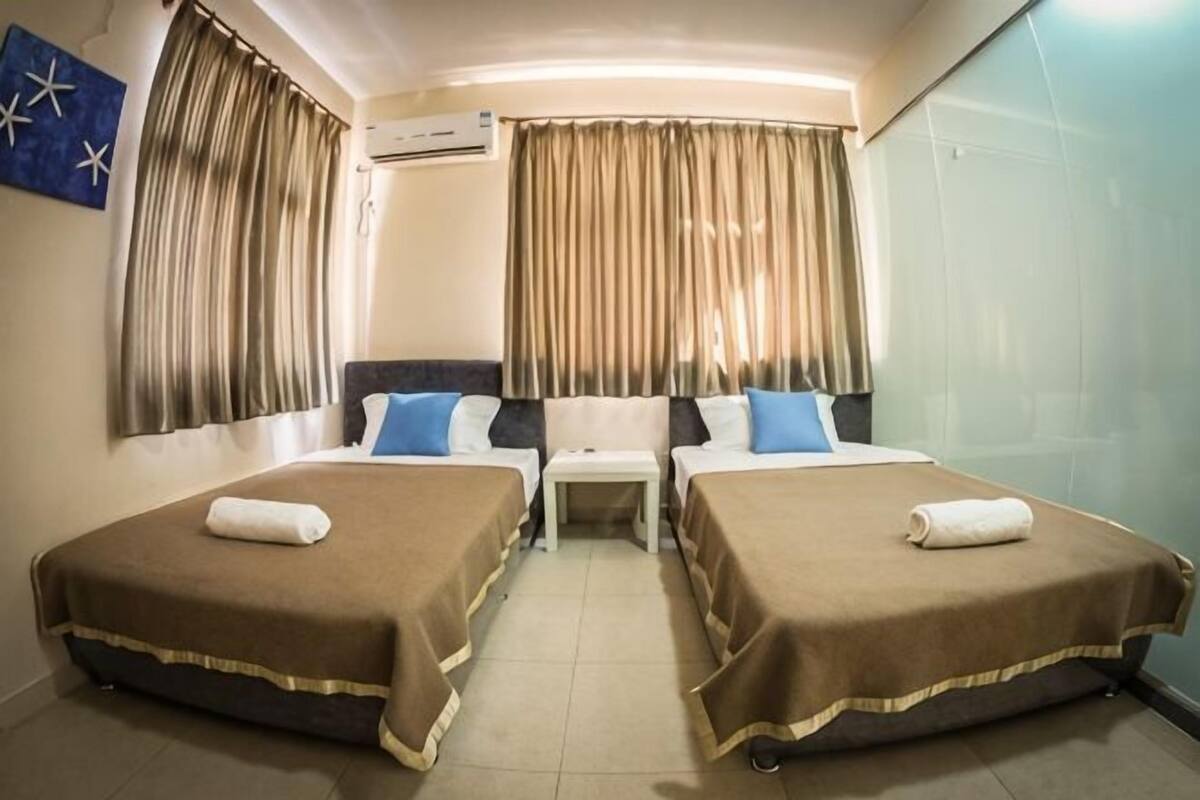 A hotel room with two beds, a small table, and curtains.