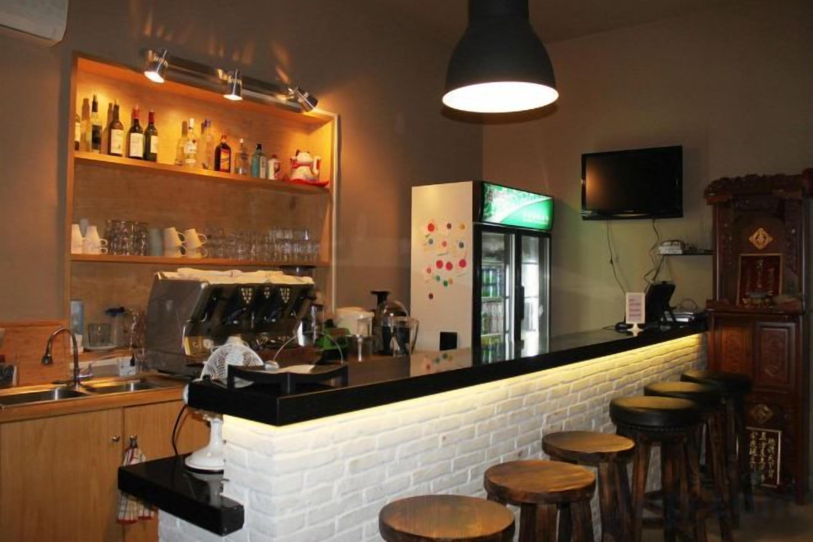 Una zona de bar con mostrador, taburetes, una máquina de café y estantes con botellas y vasos.