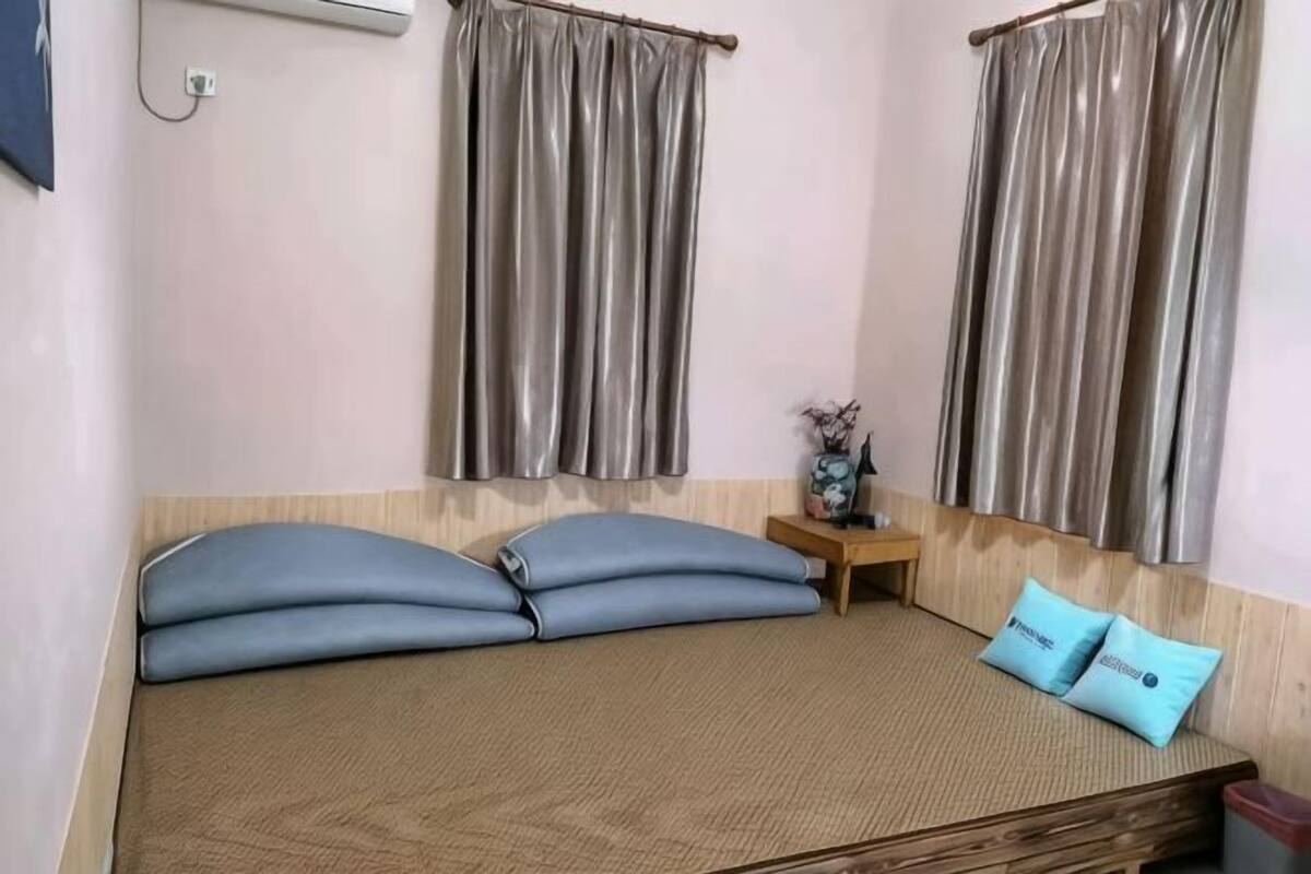 A room with a bed, two pillows, a nightstand, a vase, and curtains.