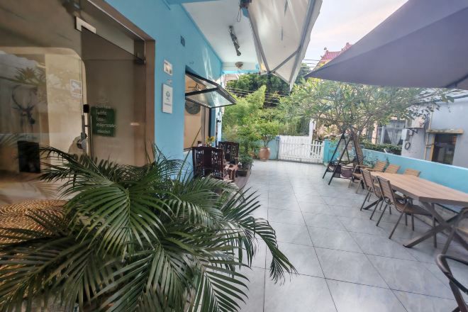 An outdoor patio area with tables and chairs, a large plant, and a blue wall.