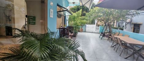 An outdoor patio area with tables and chairs, a large plant, and a blue wall.