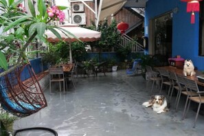 An outdoor patio with tables and chairs, a dog lying on the ground, and a hanging chair. - Hola Inn (Shenzhen)