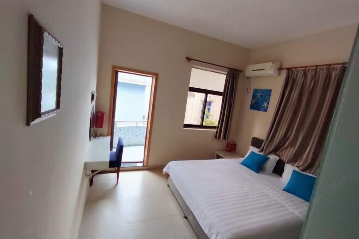 A hotel room with a bed, a window, a door, and an air conditioning unit.