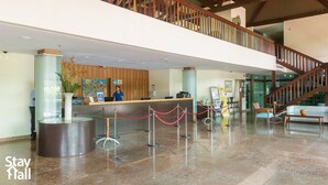 A hotel reception area with a receptionist, a reception desk, a staircase, and a glass partition. - Flat 308D Marulhos-SH058 (Ipojuca)