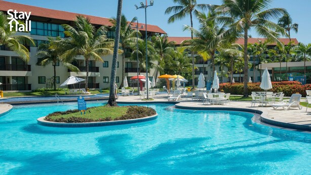 A resort pool area with palm trees, lounge chairs, and umbrellas. - Flat 308D Marulhos-SH058 (Ipojuca)