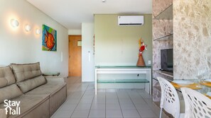 Una sala de estar moderna con un sofá color crema, una mesa de centro de vidrio, un televisor y una pared de acento de mármol.