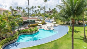 Un resort con piscina, palmeras y una zona cubierta con sombrillas.