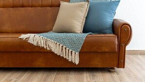 Un divano in pelle marrone con una coperta e dei cuscini beige e blu.