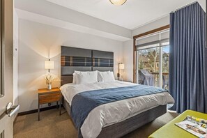 A hotel room with a large bed, two bedside lamps, a nightstand, a window with curtains, and a view of buildings outside.