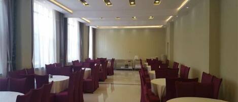 A conference room with multiple round tables and chairs, arranged in rows.