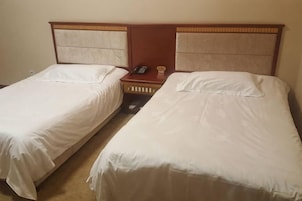 Dos camas individuales con cabeceros de madera, una mesita de noche con teléfono y un enchufe de pared.