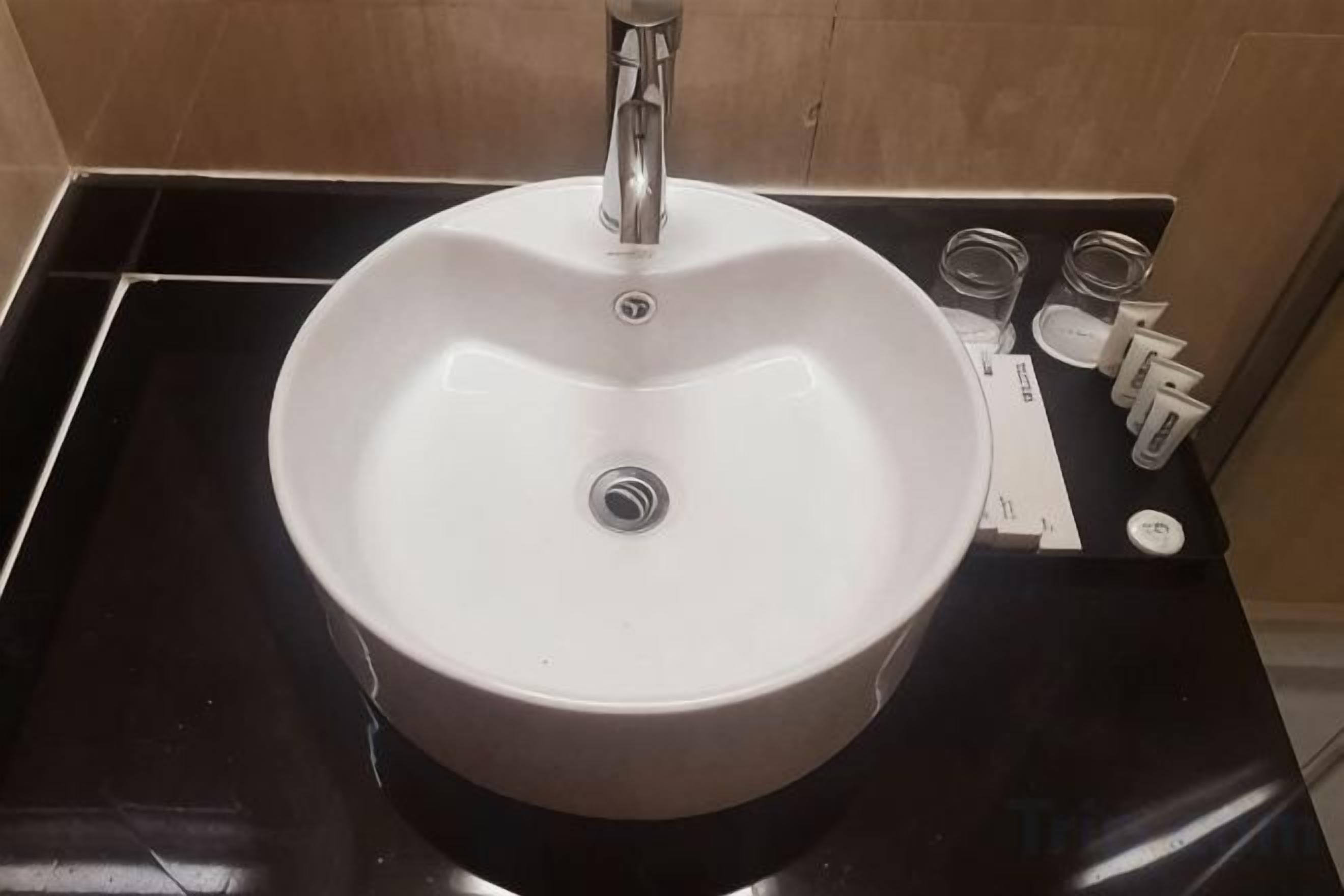 A round white sink with a faucet, a soap dispenser, and a small mirror on a black countertop.