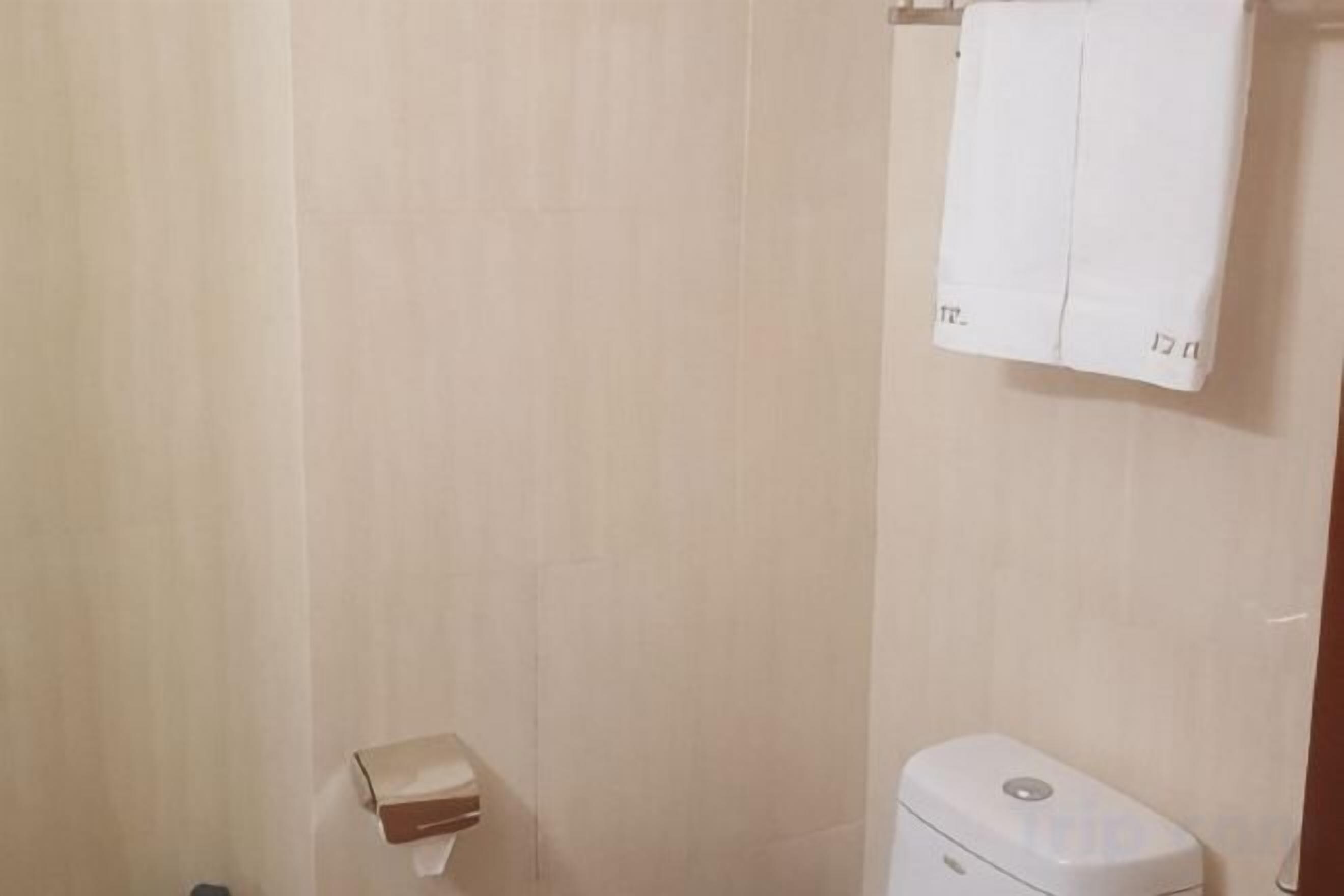 A bathroom with a toilet, a towel rack with a towel, and a small box on the floor.