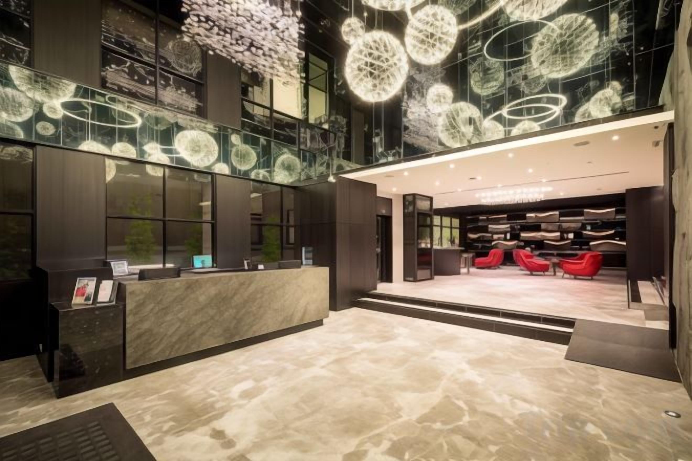 A hotel lobby with a reception desk, seating area, and decorative ceiling lights.