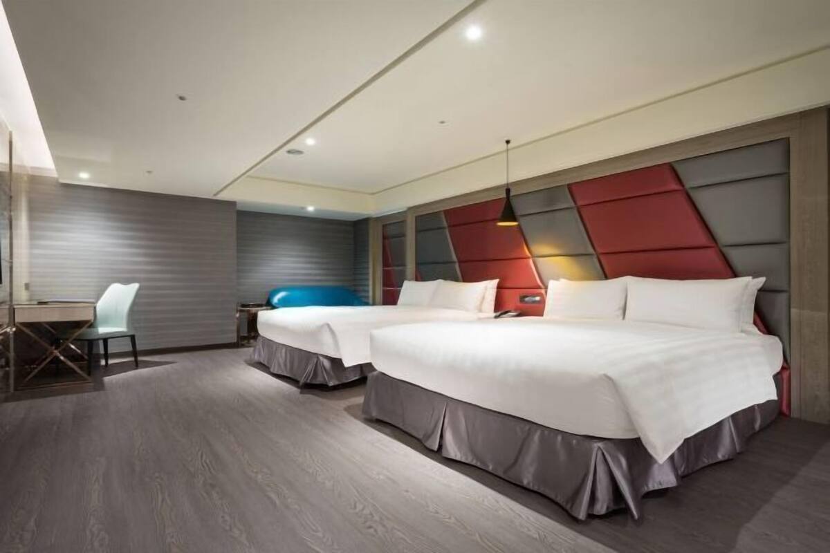 A modern hotel room with two beds, a desk, and a chair.