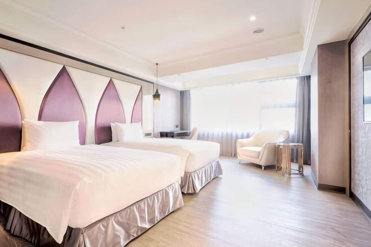 A hotel room with two beds, a desk, a chair, and a large window.