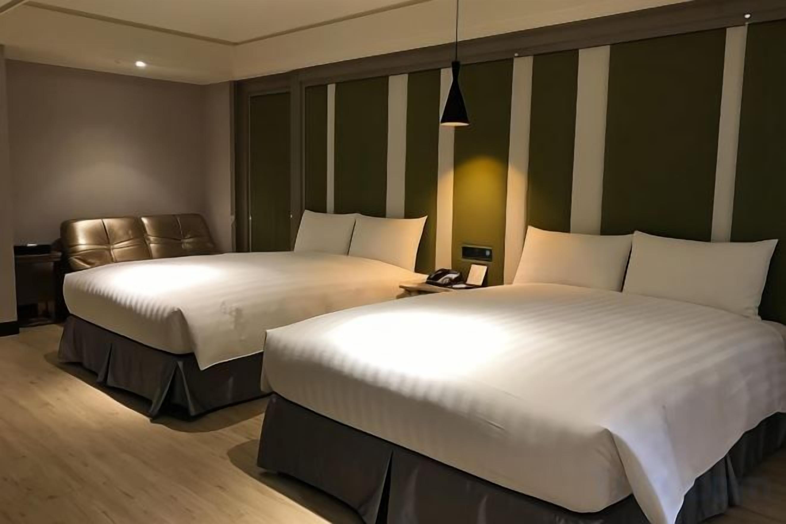 A hotel room with two beds, a nightstand, and a lamp.