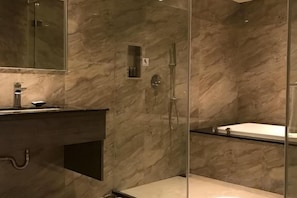 Un baño moderno con pared de mármol, cabina de ducha de vidrio y zona de aseo separada.