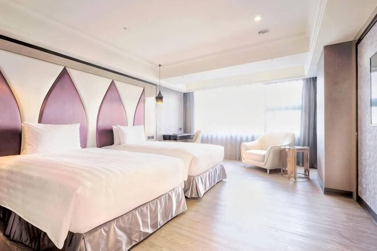 A hotel room with two beds, a desk, a chair, and a large window.