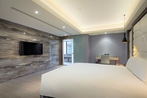 Een moderne hotelkamer met een groot bed, een flatscreen televisie aan een marmeren muur, een bureau met stoel, en een hanglamp.