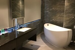 Een moderne badkamer met een vrijstaand bad, een grote spiegel en een donker aanrecht.