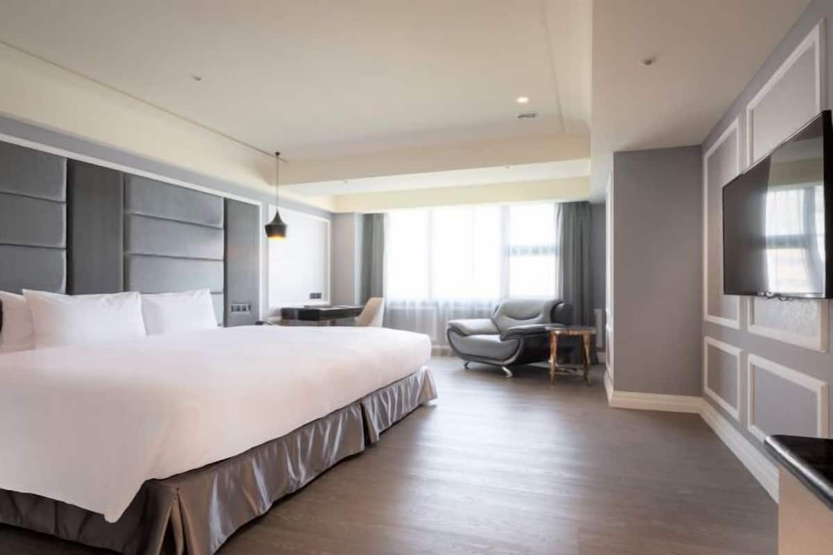A modern hotel room with a large bed, a desk, a chair, and a flat-screen TV mounted on the wall.