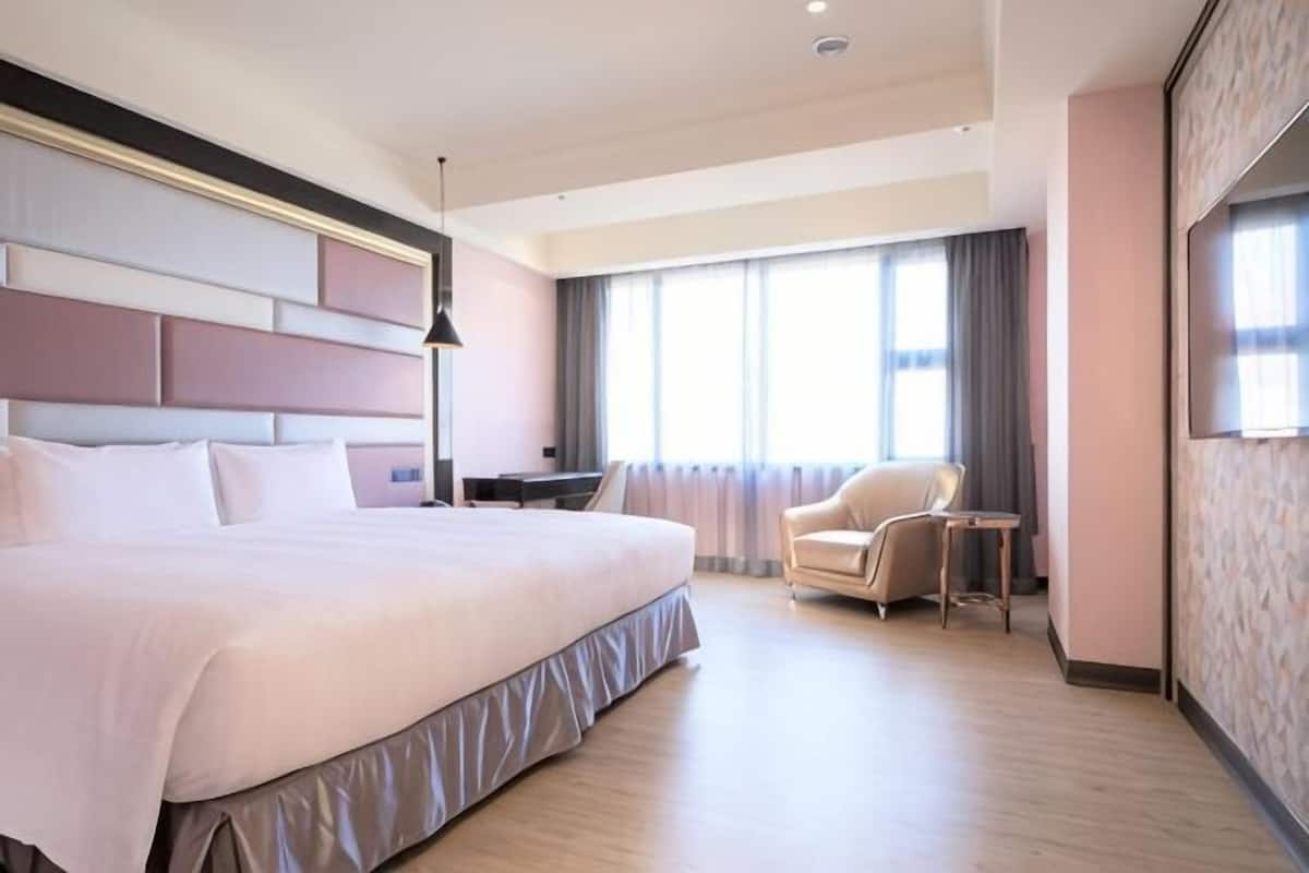 A hotel room with a large bed, a desk, a chair, and a large window.