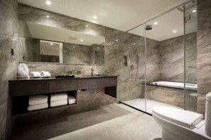 Un baño moderno con pared de mármol, cabina de ducha de vidrio, tocador de madera oscura y un espejo grande.