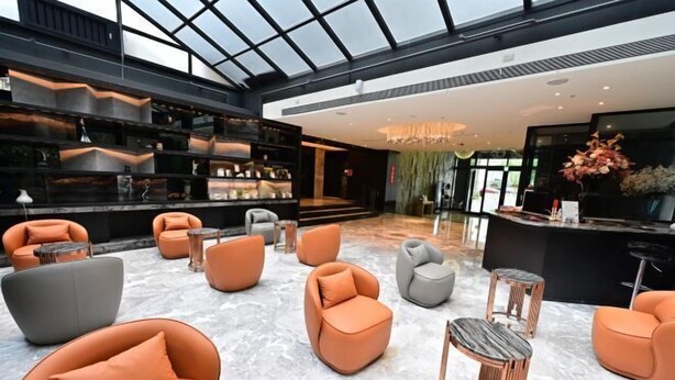 Un hall d’entrée moderne avec un plafond haut, un sol en marbre et des espaces de détente aux couleurs orange et gris.
