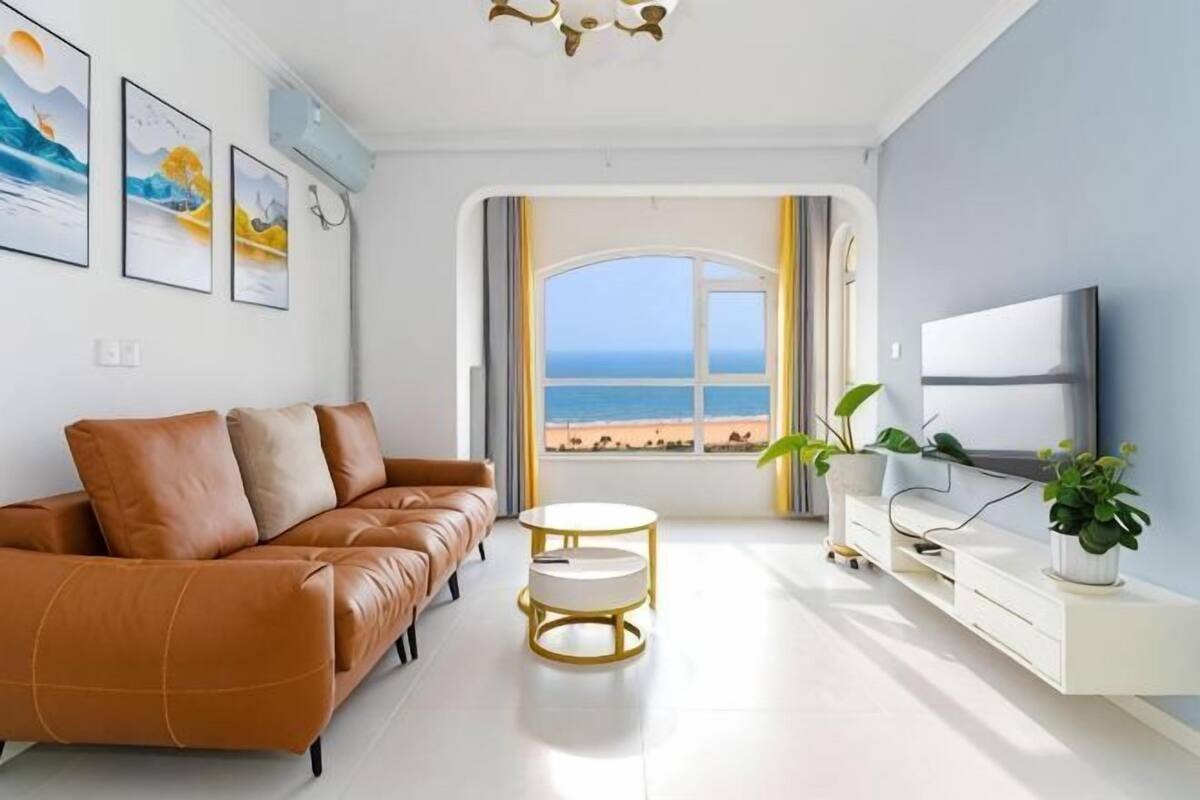 Ein modernes Wohnzimmer mit Ledersofa, Fernseher, kleinem Tisch und Blick auf den Strand.