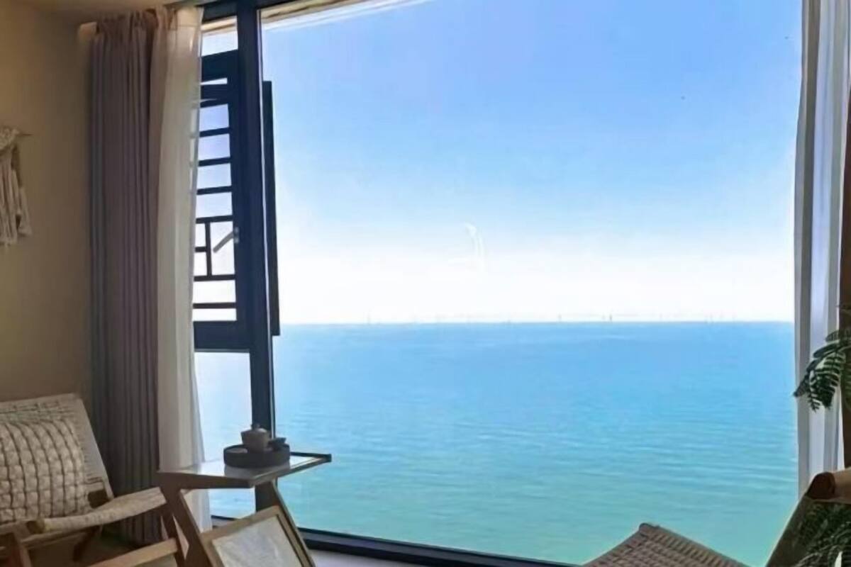 Ein Zimmer mit großem Fenster und Meerblick, ein kleiner Tisch mit Teekanne sowie ein Stuhl.