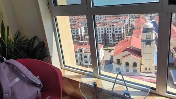 A room with a large window offering a view of a cityscape with red-roofed buildings and a clock tower.