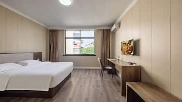 Ein Hotelzimmer mit Bett, Schreibtisch, Stuhl und einem großen Fenster mit Blick auf Gebäude.
