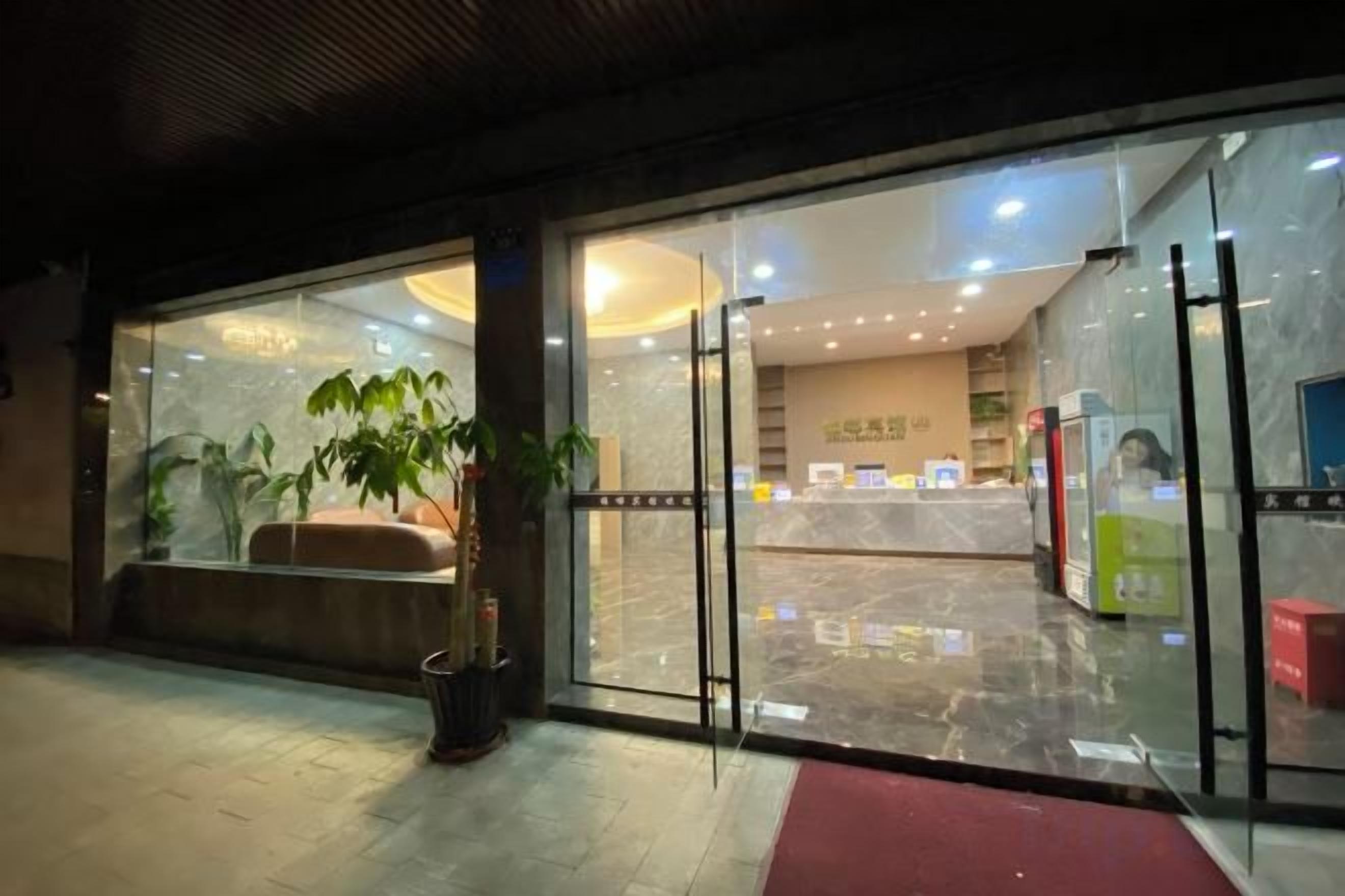 A hotel entrance with a reception desk, seating area, and a glass door.