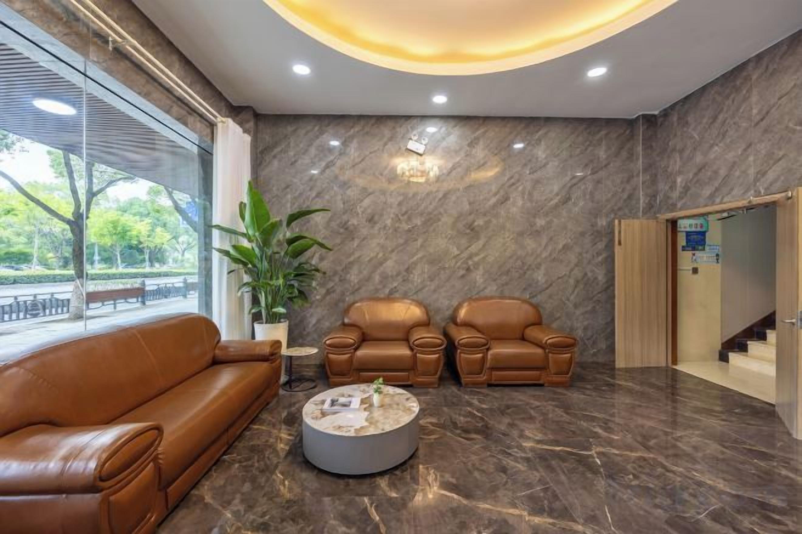 A lobby with a brown leather sofa, two armchairs, a coffee table, and a potted plant.