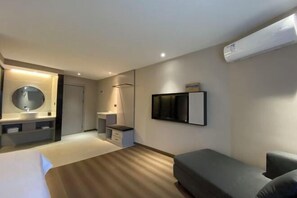 Una habitación de hotel moderna con una cama, una mesita de noche, un espejo, un televisor y un equipo de aire acondicionado.