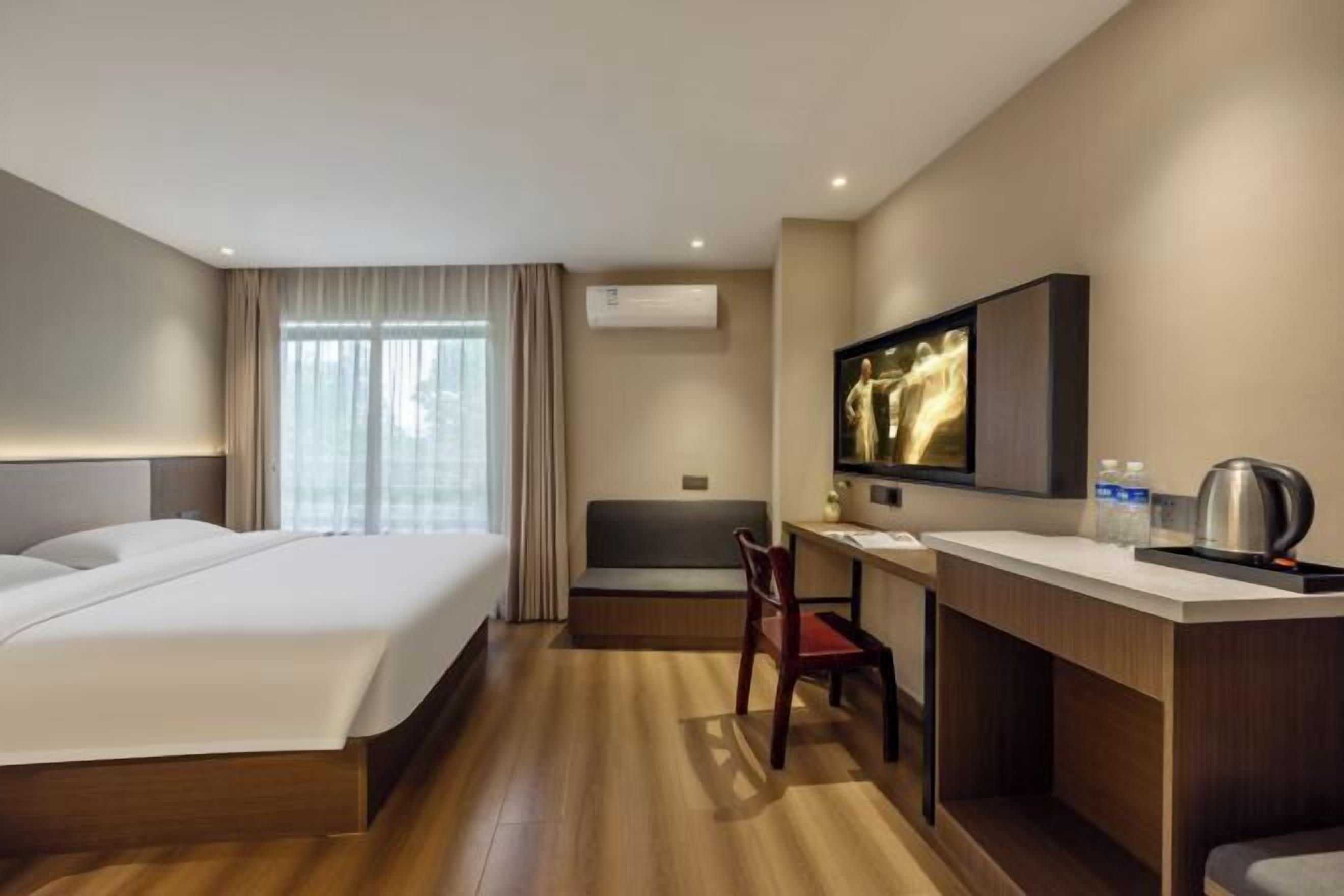 A hotel room with a bed, a desk, a chair, a television, and an air conditioning unit.