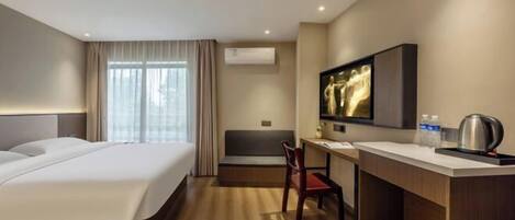 A hotel room with a bed, a desk, a chair, a television, and an air conditioning unit.