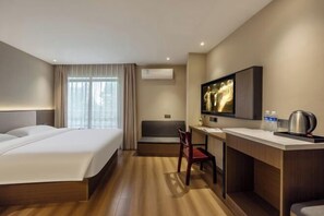 Una habitación de hotel con cama, escritorio, silla, televisión y aire acondicionado.