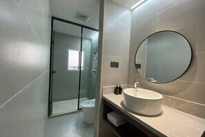 Un baño moderno con ducha envuelta en vidrio, un espejo redondo y un lavabo blanco.