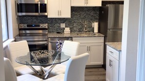A modern kitchen with white cabinets, stainless steel appliances, and a glass dining table with white chairs.