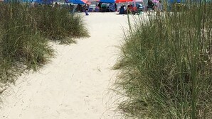 A beach path leading to beach umbrellas and beachgoers.