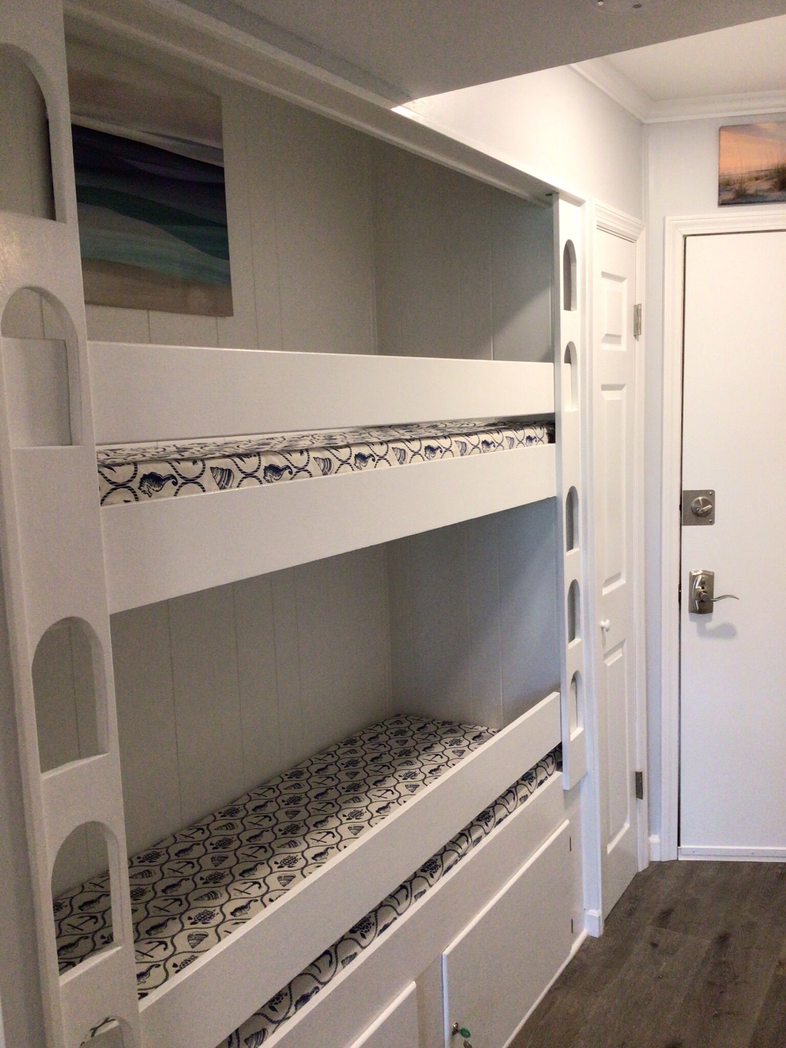 A bunk bed with patterned bedding in a room with a door and a painting on the wall.