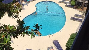 A swimming pool with lounge chairs and umbrellas, surrounded by trees and a fence.