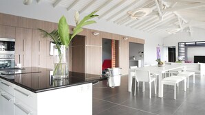 A modern kitchen with a central island, white cabinetry, and a dining area with white chairs and a table. - Very nice villa Indigo overlooking golf court (Saint François)