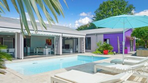 A pool area with lounge chairs, a covered seating area, and a purple building. - Very nice villa Indigo overlooking golf court (Saint François)